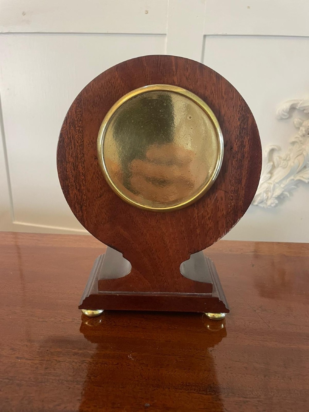 An Edwardian mahogany mantle clock featuring floral satinwood inlay, a white dial with Roman numerals, a brass bezel, and small brass bun feet. View III