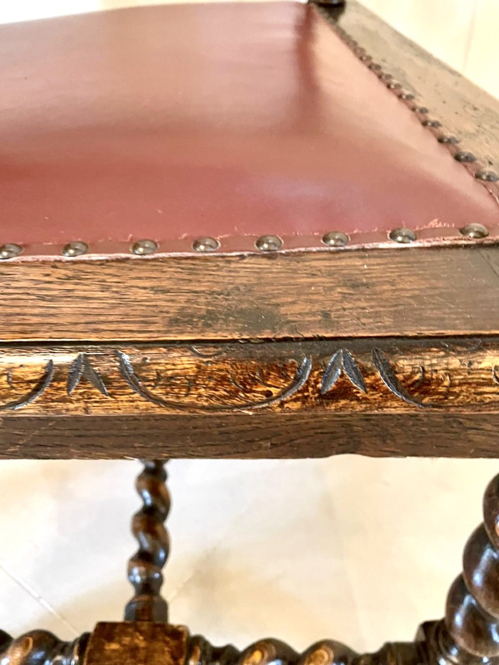 A high-backed Victorian carved oak armchair featuring barley twist supports, acanthus leaf carvings, and a burgundy leather seat with brass stud detail. View II