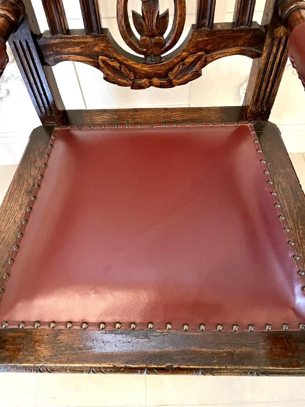 A high-backed Victorian carved oak armchair featuring barley twist supports, acanthus leaf carvings, and a burgundy leather seat with brass stud detail. View IV