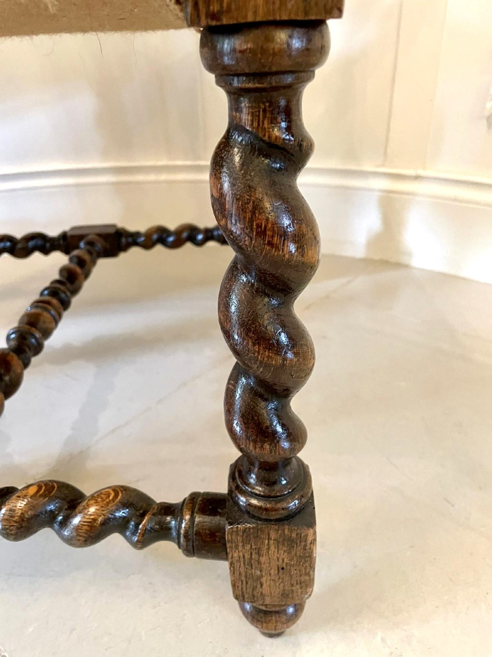 A high-backed Victorian carved oak armchair featuring barley twist supports, acanthus leaf carvings, and a burgundy leather seat with brass stud detail. View V