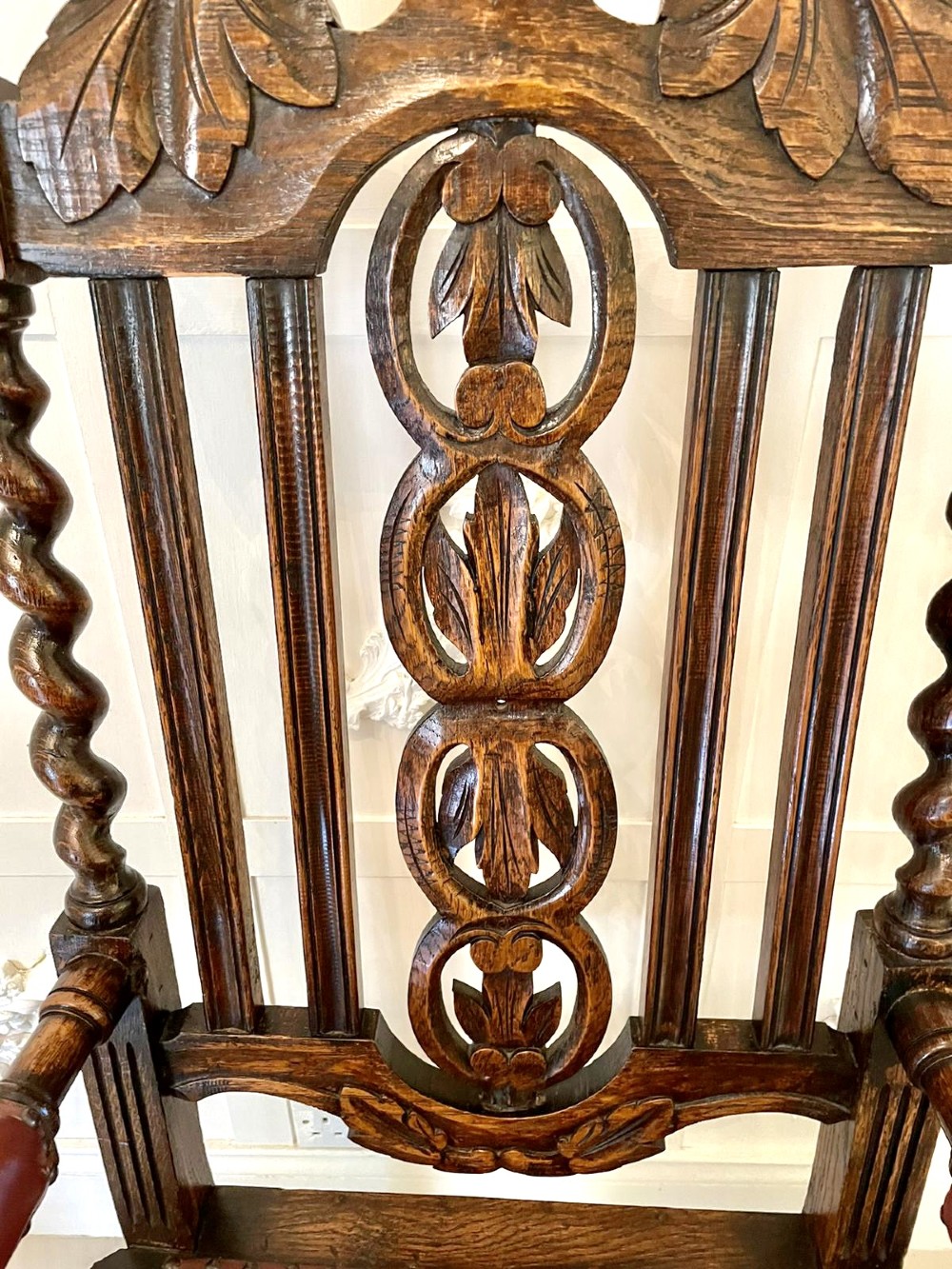 A high-backed Victorian carved oak armchair featuring barley twist supports, acanthus leaf carvings, and a burgundy leather seat with brass stud detail. View VII