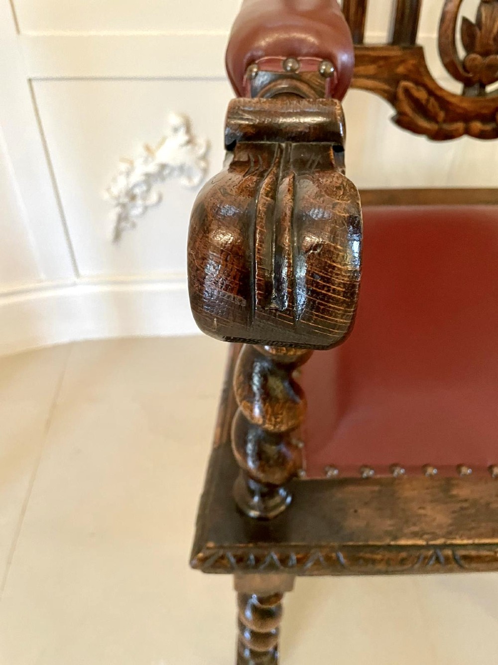 A high-backed Victorian carved oak armchair featuring barley twist supports, acanthus leaf carvings, and a burgundy leather seat with brass stud detail. View IX