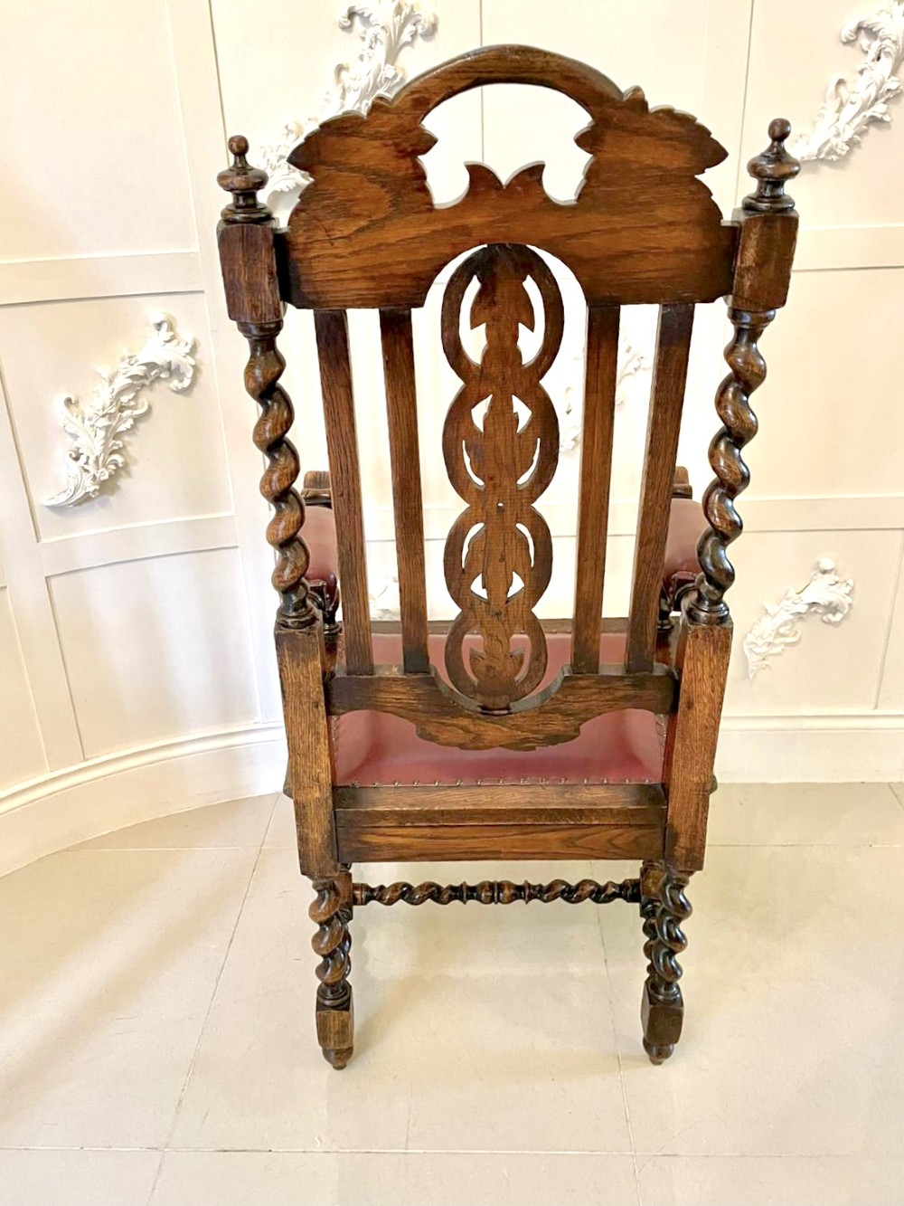 A high-backed Victorian carved oak armchair featuring barley twist supports, acanthus leaf carvings, and a burgundy leather seat with brass stud detail. View X