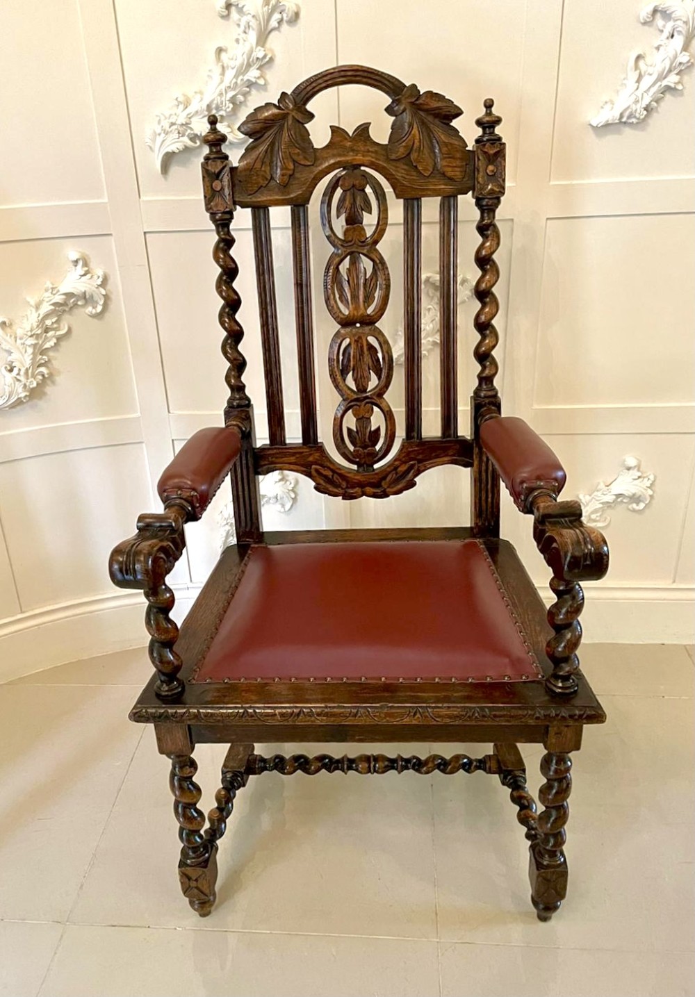 A high-backed Victorian carved oak armchair featuring barley twist supports, acanthus leaf carvings, and a burgundy leather seat with brass stud detail. View XI