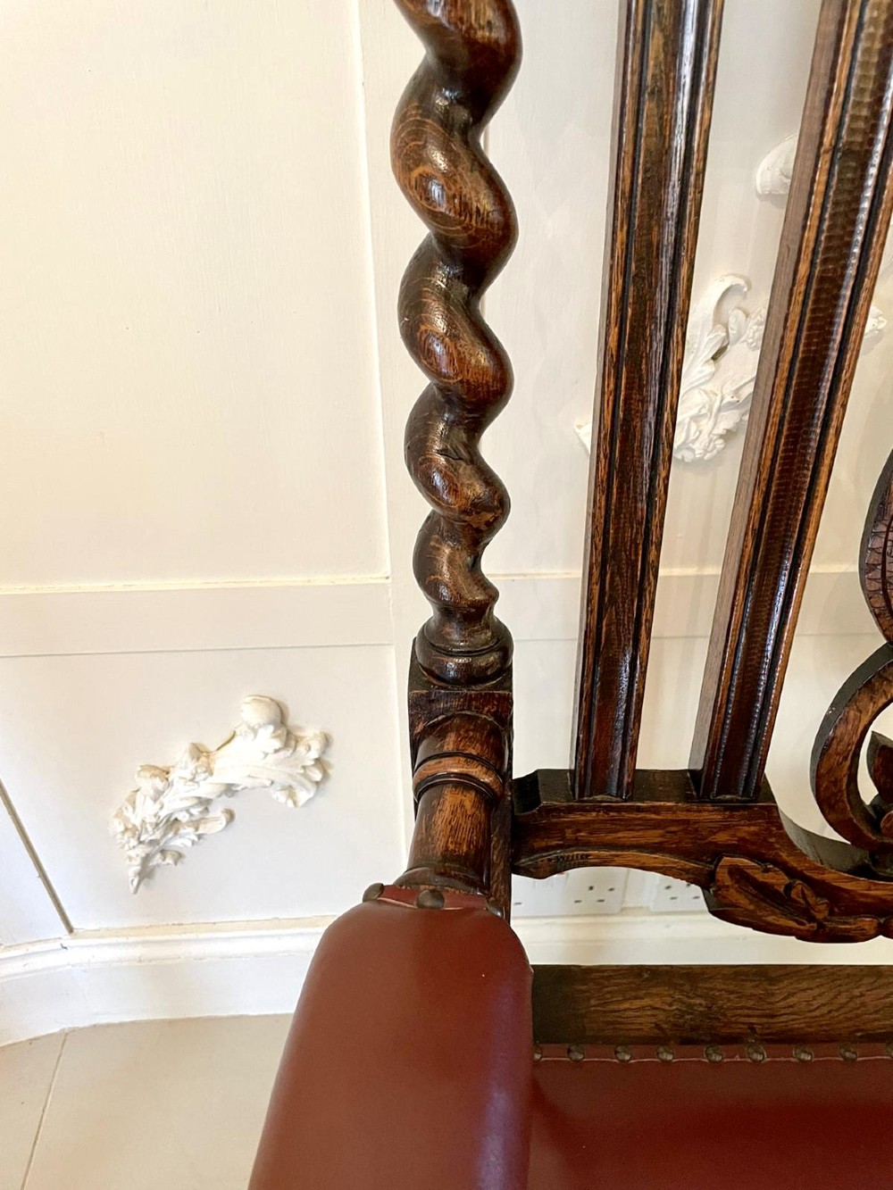 A high-backed Victorian carved oak armchair featuring barley twist supports, acanthus leaf carvings, and a burgundy leather seat with brass stud detail. View XII