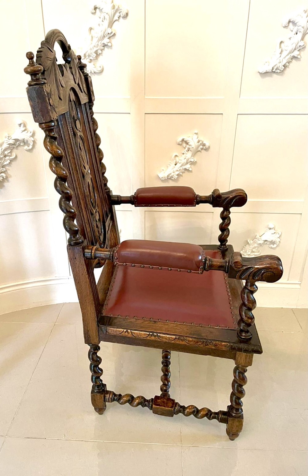 A high-backed Victorian carved oak armchair featuring barley twist supports, acanthus leaf carvings, and a burgundy leather seat with brass stud detail. View XIII