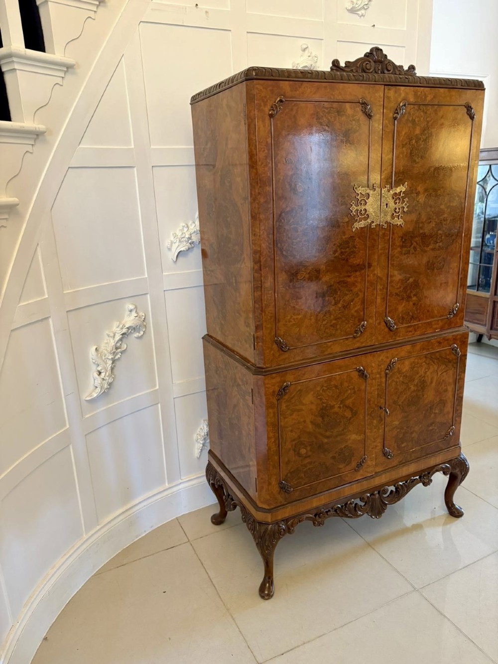 An antique burr walnut cocktail cabinet featuring two upper doors with ornate brass hardware, set on carved cabriole legs. View VI