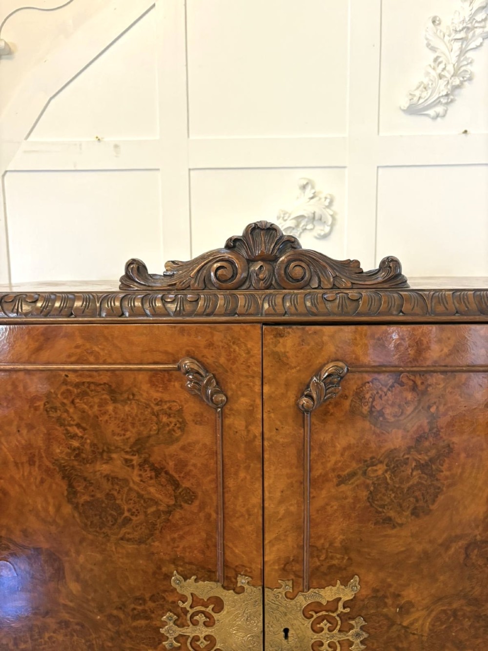 An antique burr walnut cocktail cabinet featuring two upper doors with ornate brass hardware, set on carved cabriole legs. View VII
