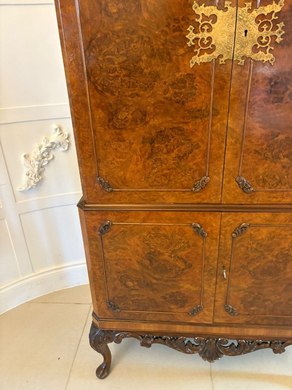 An antique burr walnut cocktail cabinet featuring two upper doors with ornate brass hardware, set on carved cabriole legs. View IX