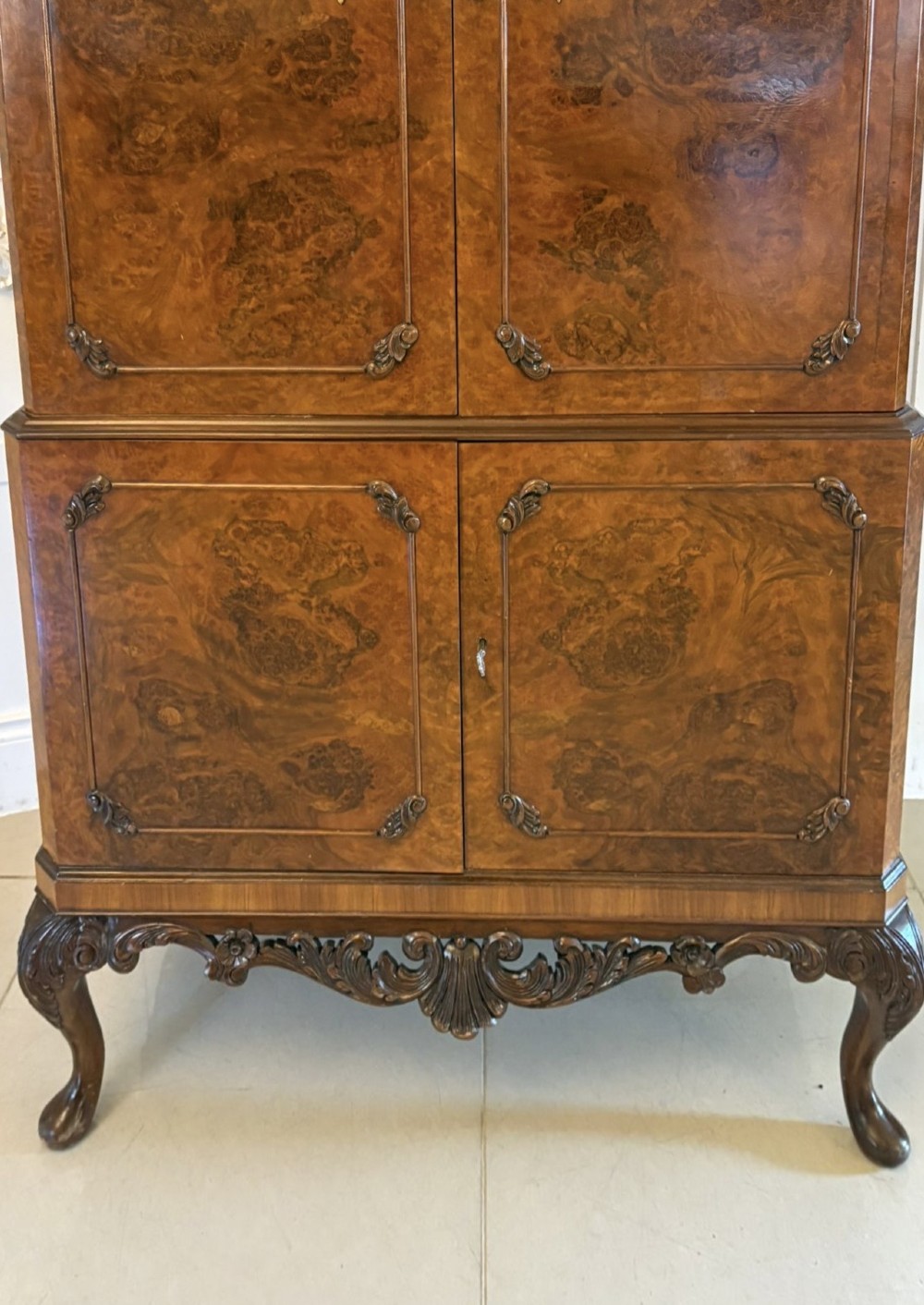An antique burr walnut cocktail cabinet featuring two upper doors with ornate brass hardware, set on carved cabriole legs. View X
