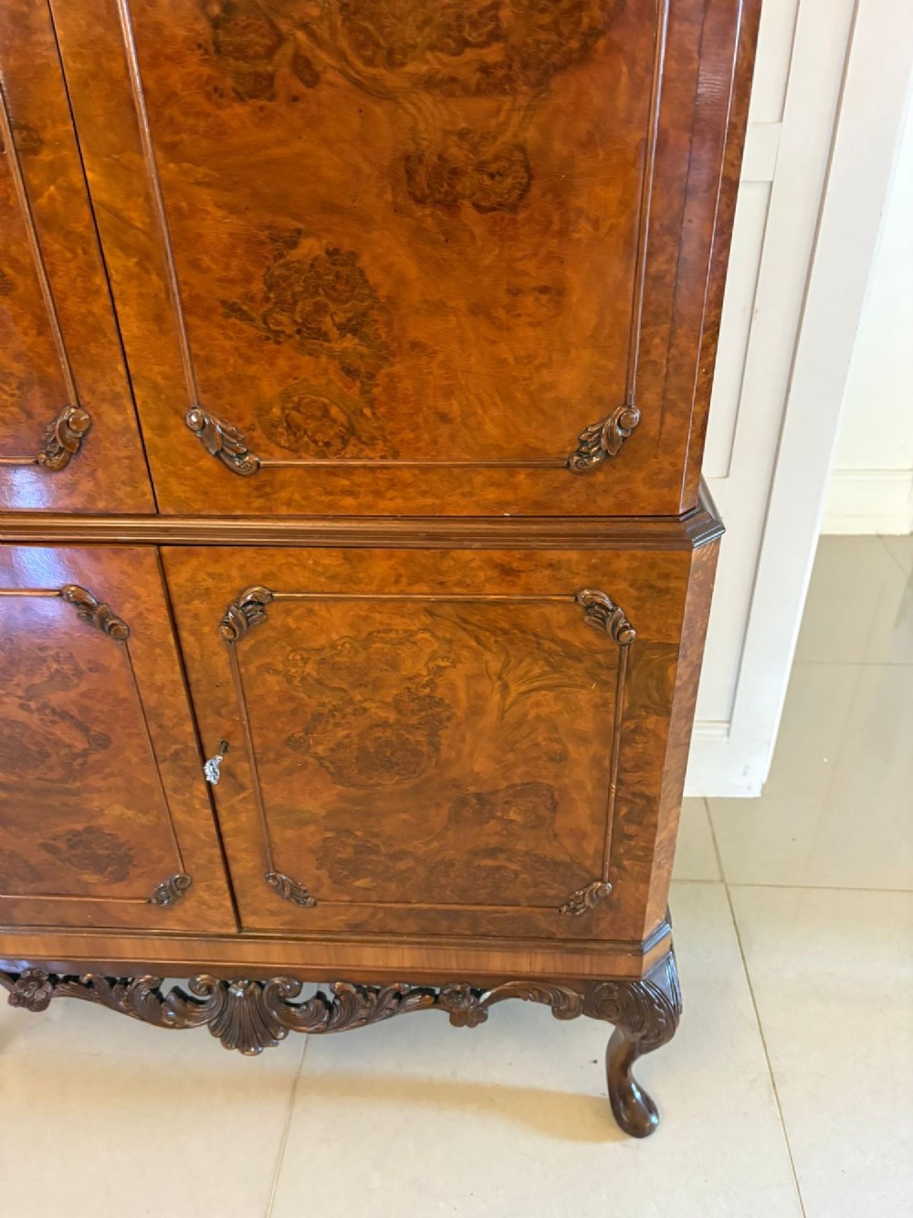 An antique burr walnut cocktail cabinet featuring two upper doors with ornate brass hardware, set on carved cabriole legs. View XII