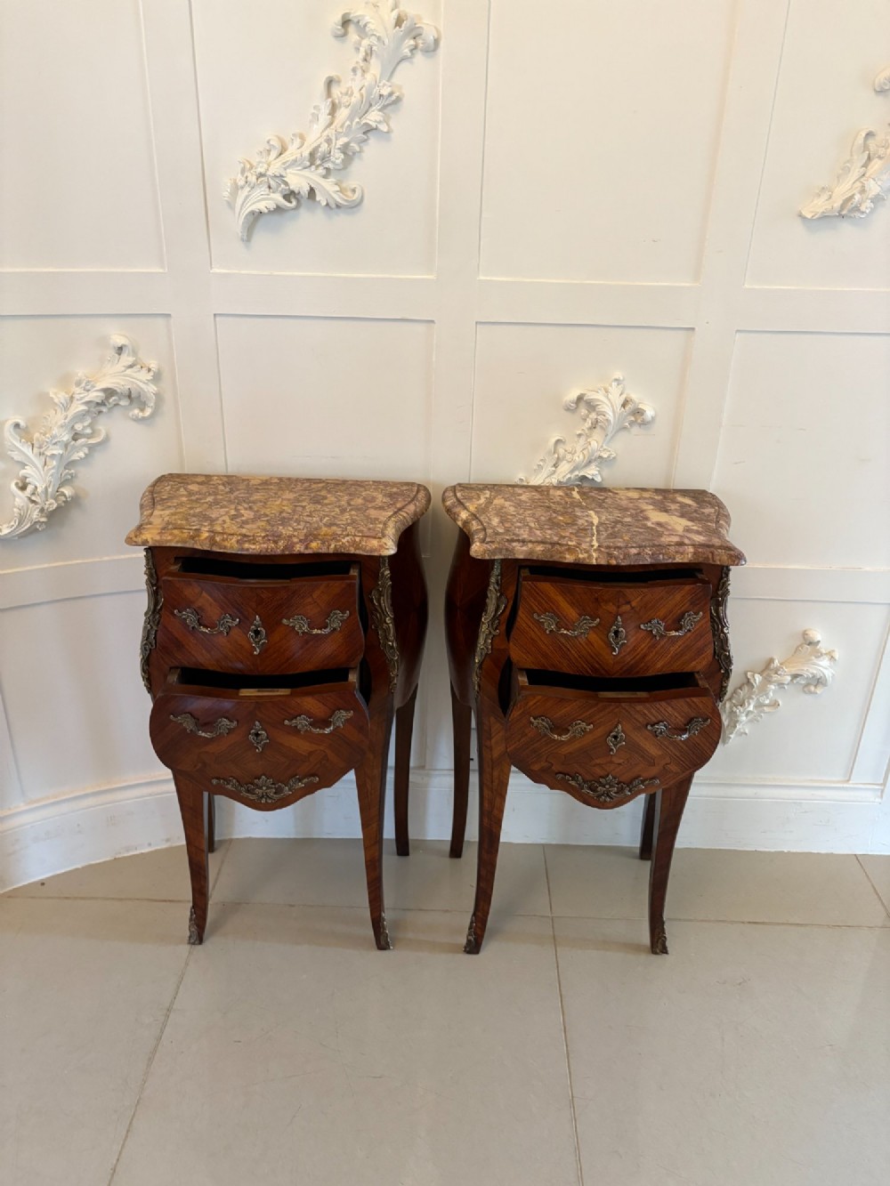 A pair of French Louis XV style kingwood bedside cabinets featuring two drawers, marquetry inlay, gilt bronze mounts, and serpentine marble tops. View IV