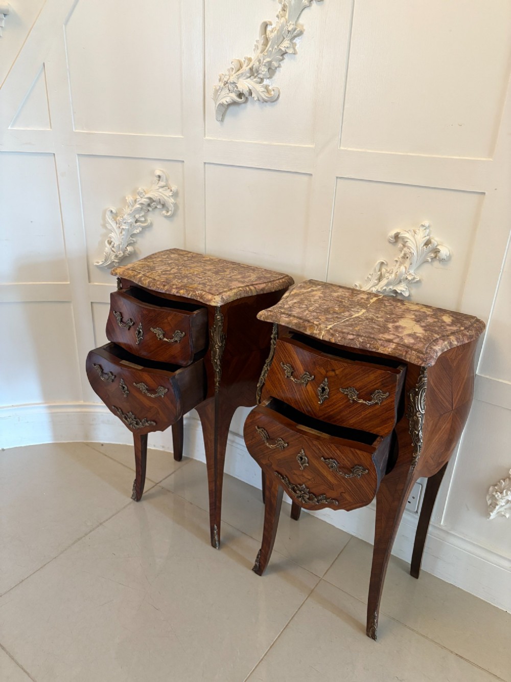 A pair of French Louis XV style kingwood bedside cabinets featuring two drawers, marquetry inlay, gilt bronze mounts, and serpentine marble tops. View V