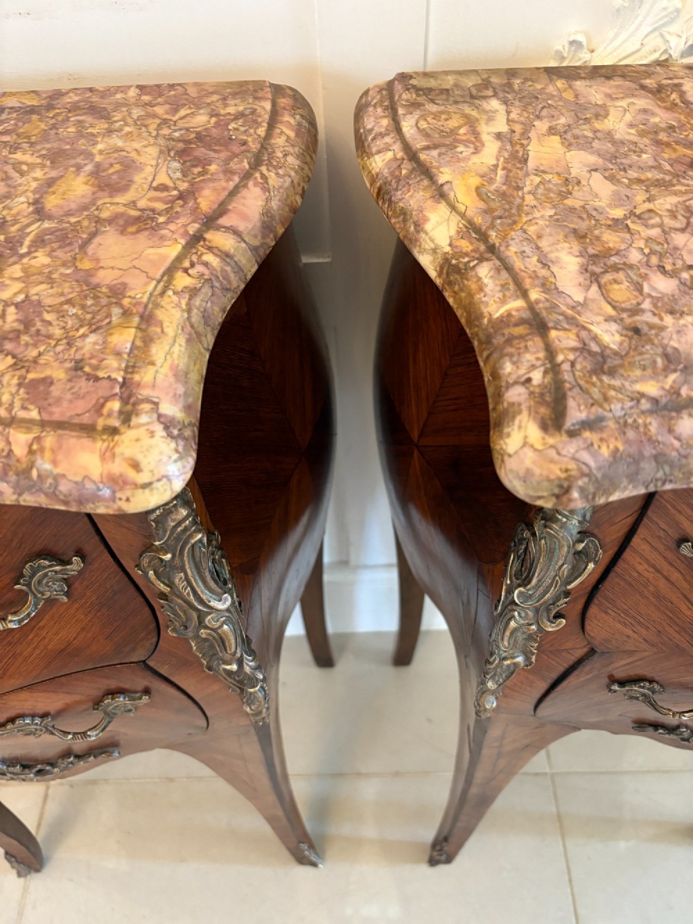 A pair of French Louis XV style kingwood bedside cabinets featuring two drawers, marquetry inlay, gilt bronze mounts, and serpentine marble tops. View VI