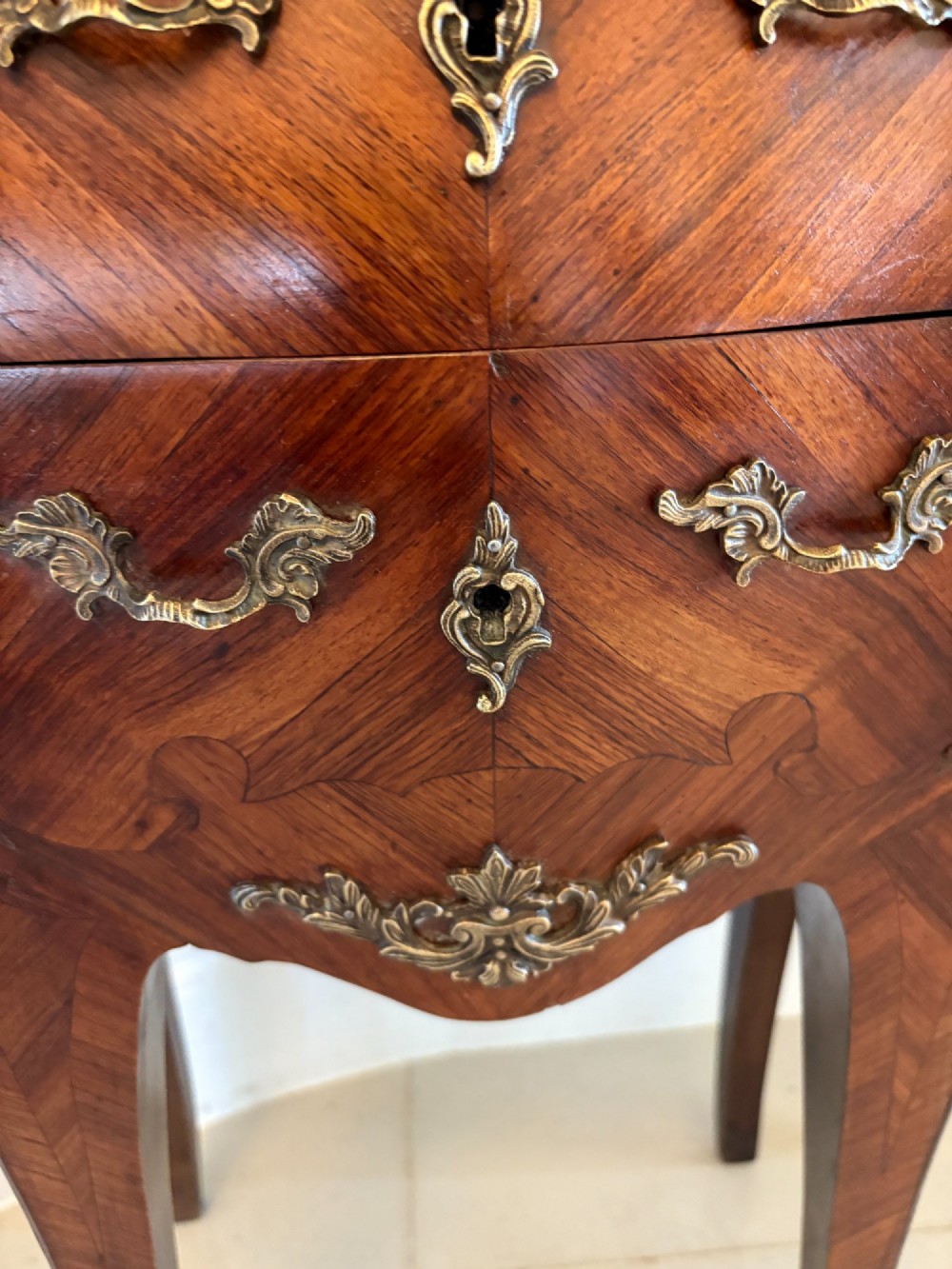 A pair of French Louis XV style kingwood bedside cabinets featuring two drawers, marquetry inlay, gilt bronze mounts, and serpentine marble tops. View IX
