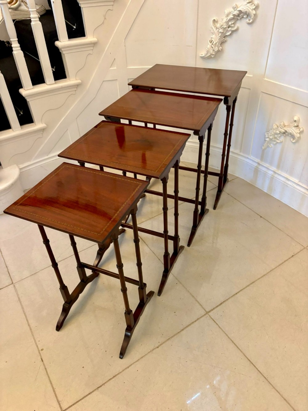 A set of four graduated Edwardian mahogany nesting tables featuring fine satinwood inlay borders and slender turned legs on trestle feet.