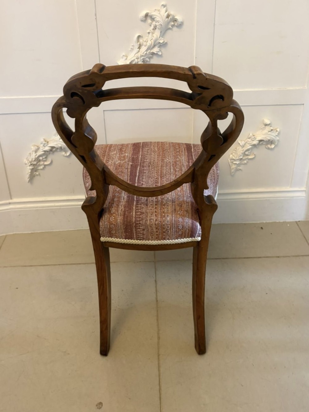 A set of four Victorian walnut balloon back dining chairs featuring carved openwork backrests, cabriole front legs, and patterned rose-coloured upholstered seats. View VI