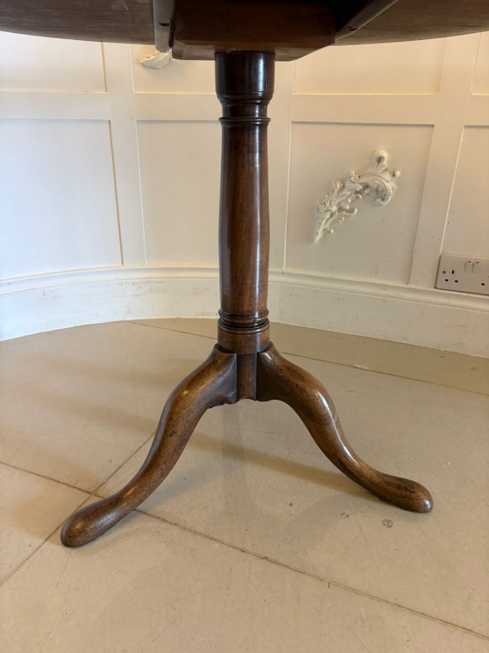 An 18th-century Georgian circular mahogany tilt-top table shown with its surface tilted vertically on a turned column with three cabriole legs. View VI