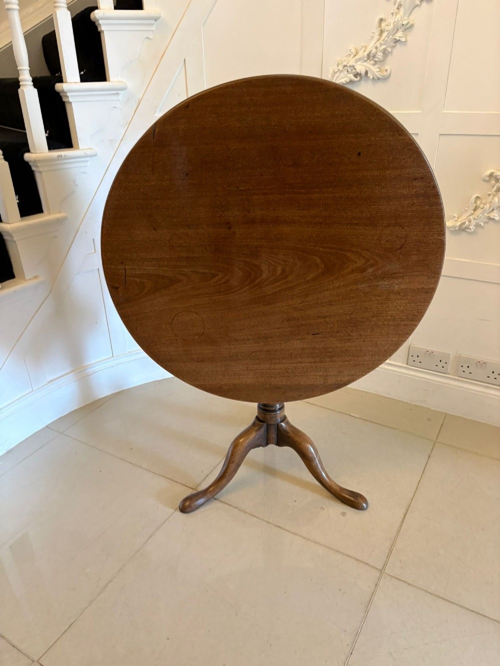 An 18th-century Georgian circular mahogany tilt-top table shown with its surface tilted vertically on a turned column with three cabriole legs.