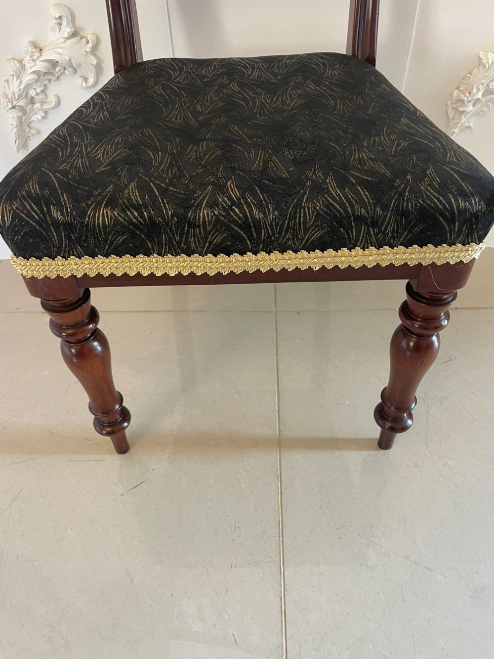 A set of ten Victorian mahogany dining chairs with curved crest rails, turned front legs, and dark pattern upholstered seats. View II