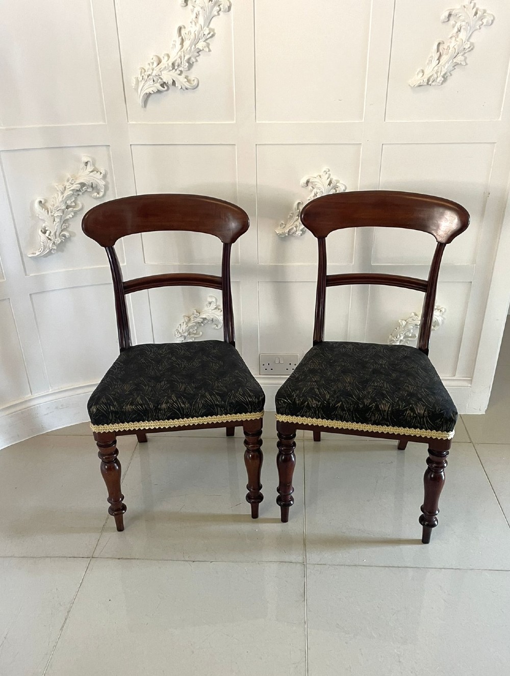 A set of ten Victorian mahogany dining chairs with curved crest rails, turned front legs, and dark pattern upholstered seats. View VI