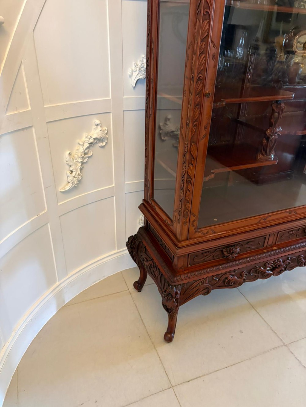 A carved reddish-brown hardwood display cabinet featuring a pagoda cresting, glass door, asymmetrical interior shelves, lower drawers, and cabriole legs. View VII