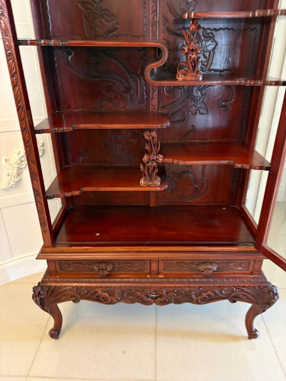 A carved reddish-brown hardwood display cabinet featuring a pagoda cresting, glass door, asymmetrical interior shelves, lower drawers, and cabriole legs. View IX