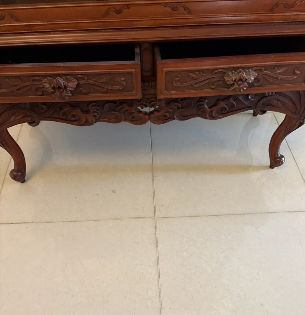 A carved reddish-brown hardwood display cabinet featuring a pagoda cresting, glass door, asymmetrical interior shelves, lower drawers, and cabriole legs. View X