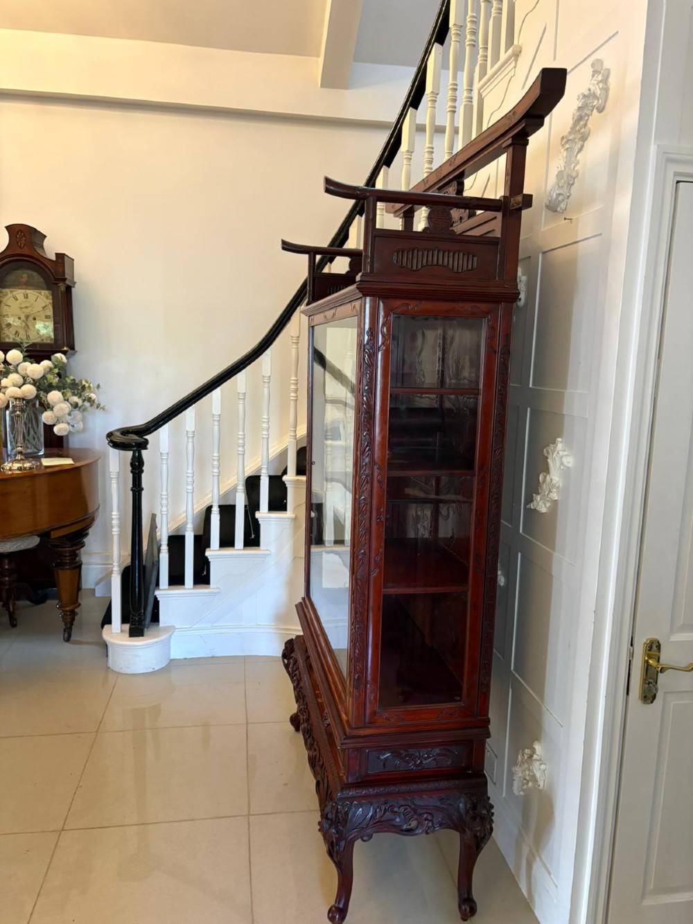 A carved reddish-brown hardwood display cabinet featuring a pagoda cresting, glass door, asymmetrical interior shelves, lower drawers, and cabriole legs. View XII