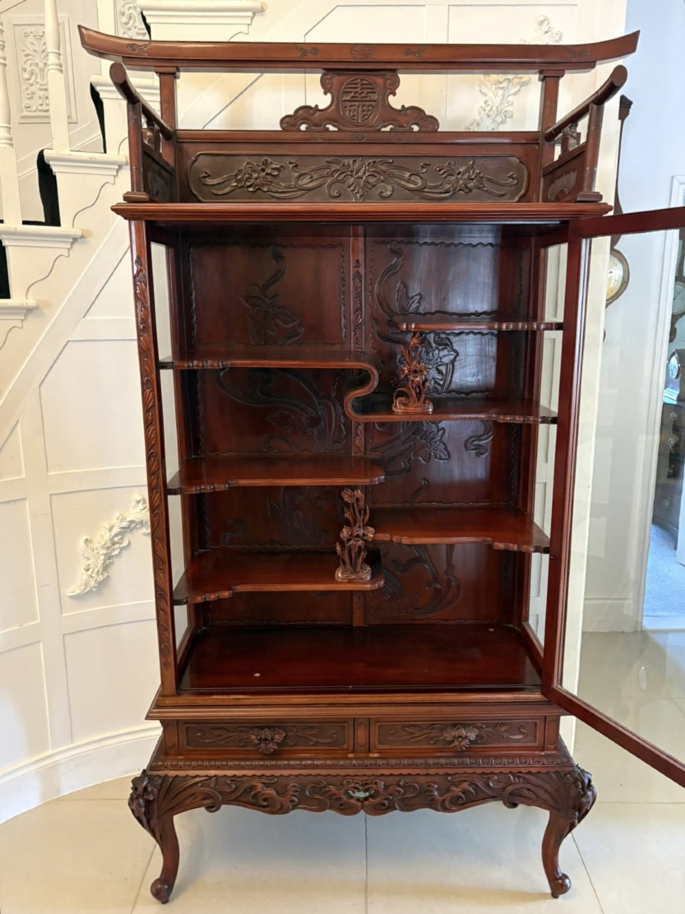 A carved reddish-brown hardwood display cabinet featuring a pagoda cresting, glass door, asymmetrical interior shelves, lower drawers, and cabriole legs. View XIII