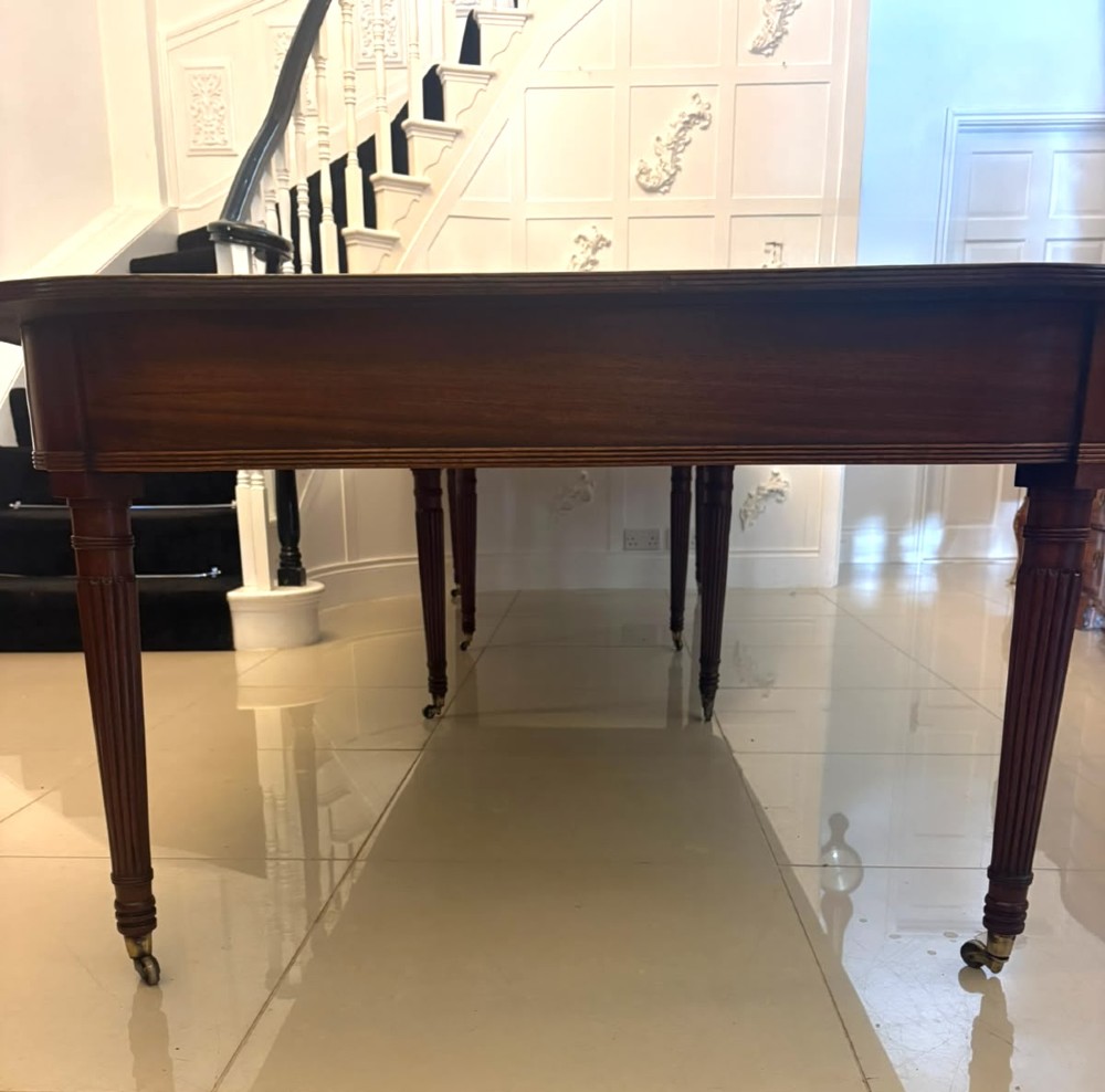 A long Regency extending dining table crafted from polished figured mahogany with reeded legs set on brass castors. View XIII