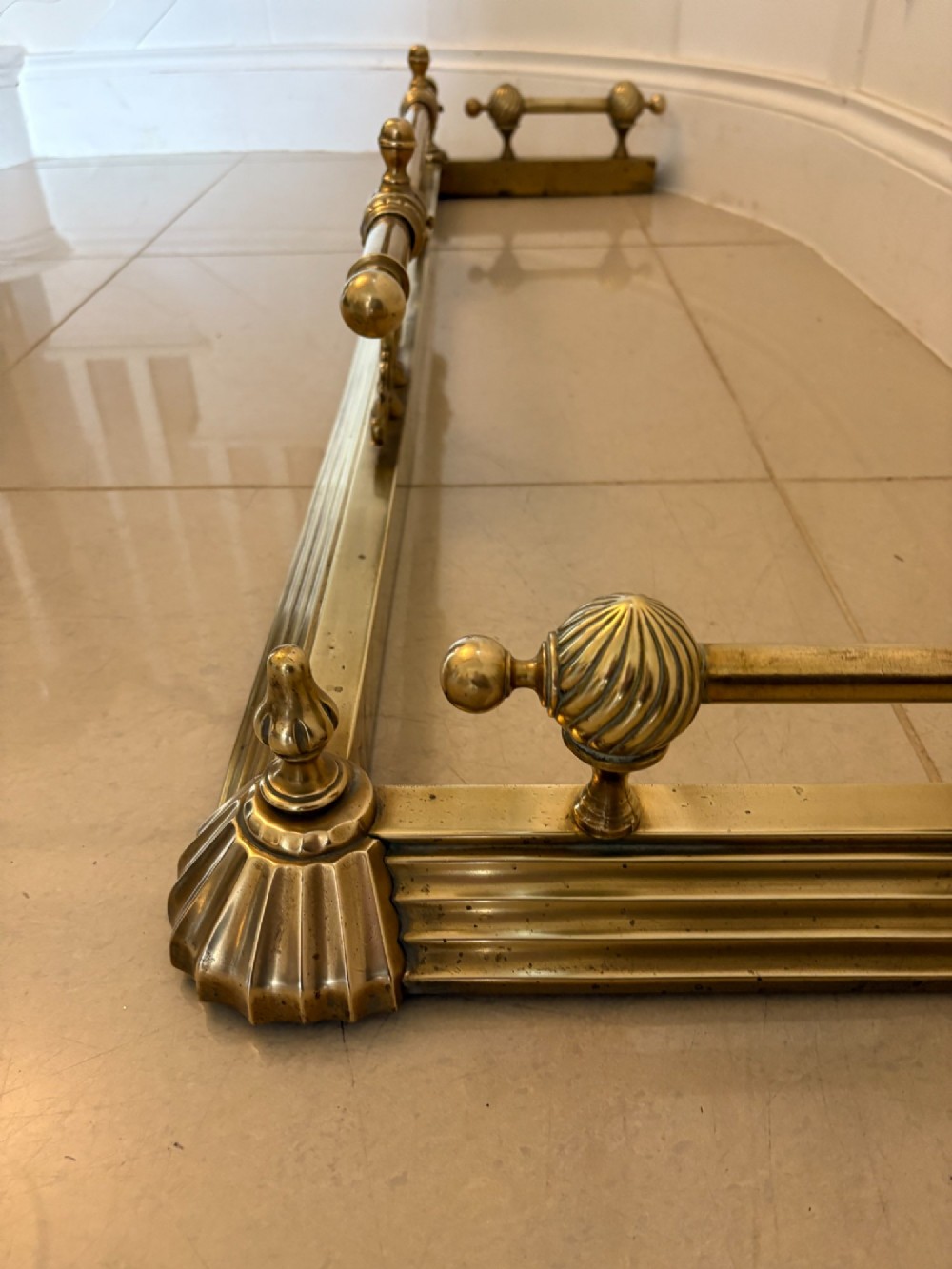 An antique Victorian brass fireplace fender featuring a central raised rail, turned finials, and a moulded lower base. View III