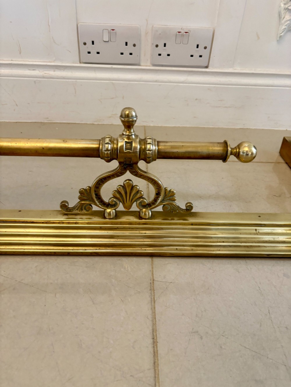 An antique Victorian brass fireplace fender featuring a central raised rail, turned finials, and a moulded lower base. View IV