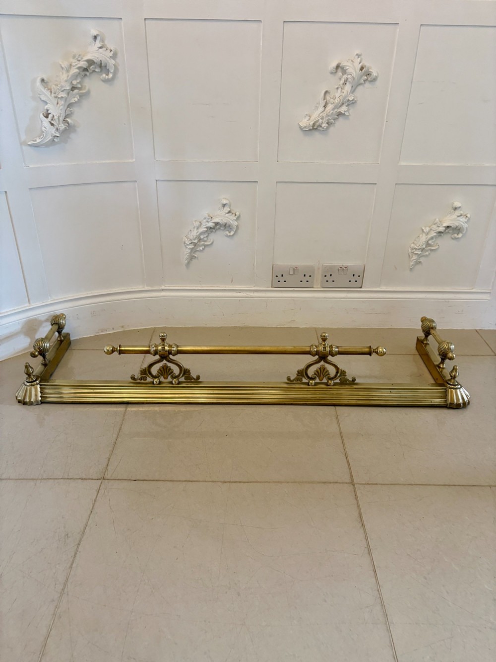 An antique Victorian brass fireplace fender featuring a central raised rail, turned finials, and a moulded lower base. View VIII