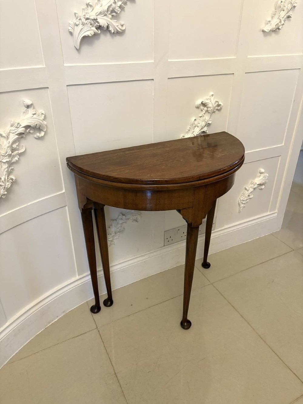 An antique warm brown mahogany demi-lune card table featuring tapered legs with pad feet and a fold-over top. View III