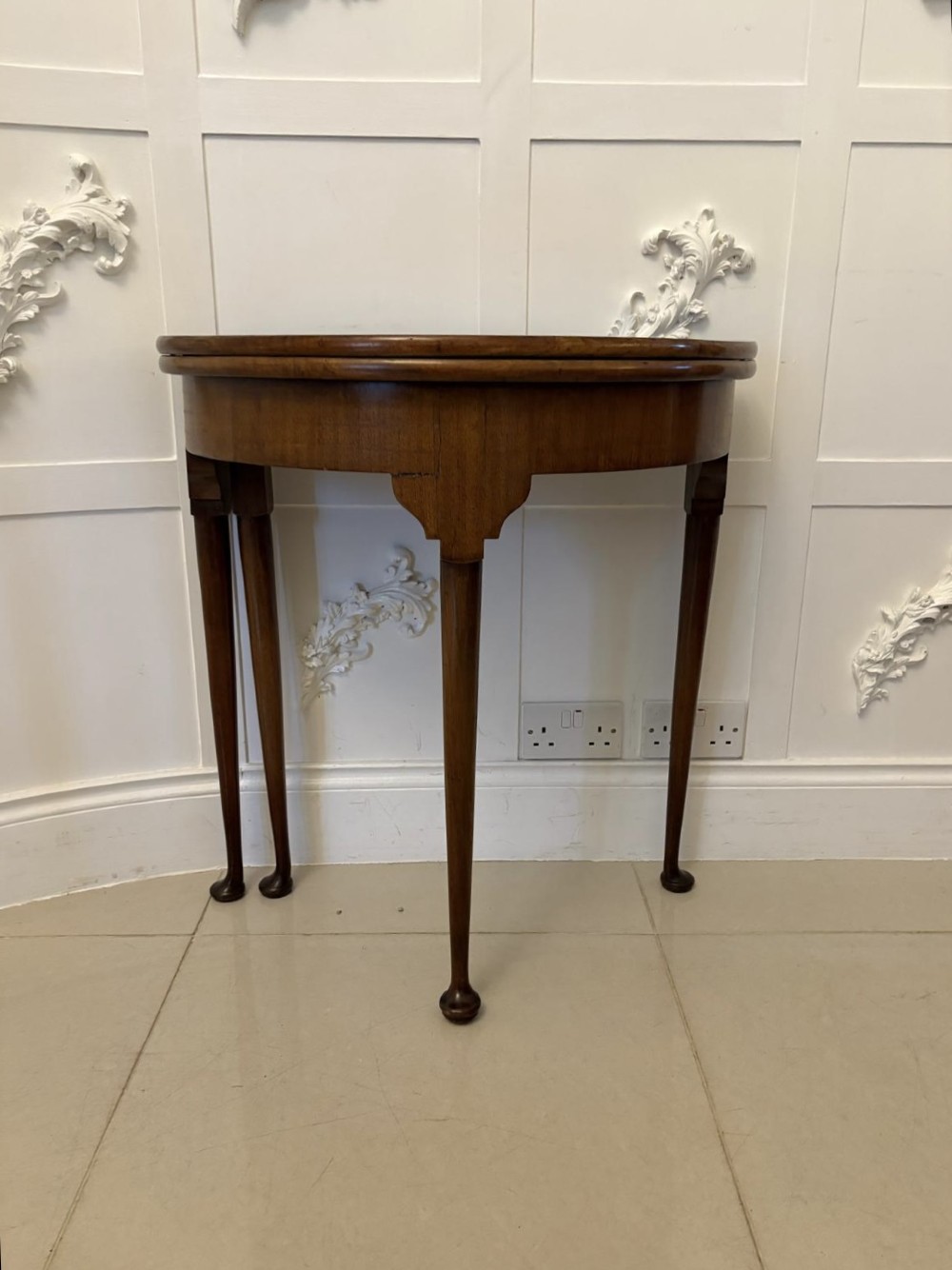 An antique warm brown mahogany demi-lune card table featuring tapered legs with pad feet and a fold-over top. View V