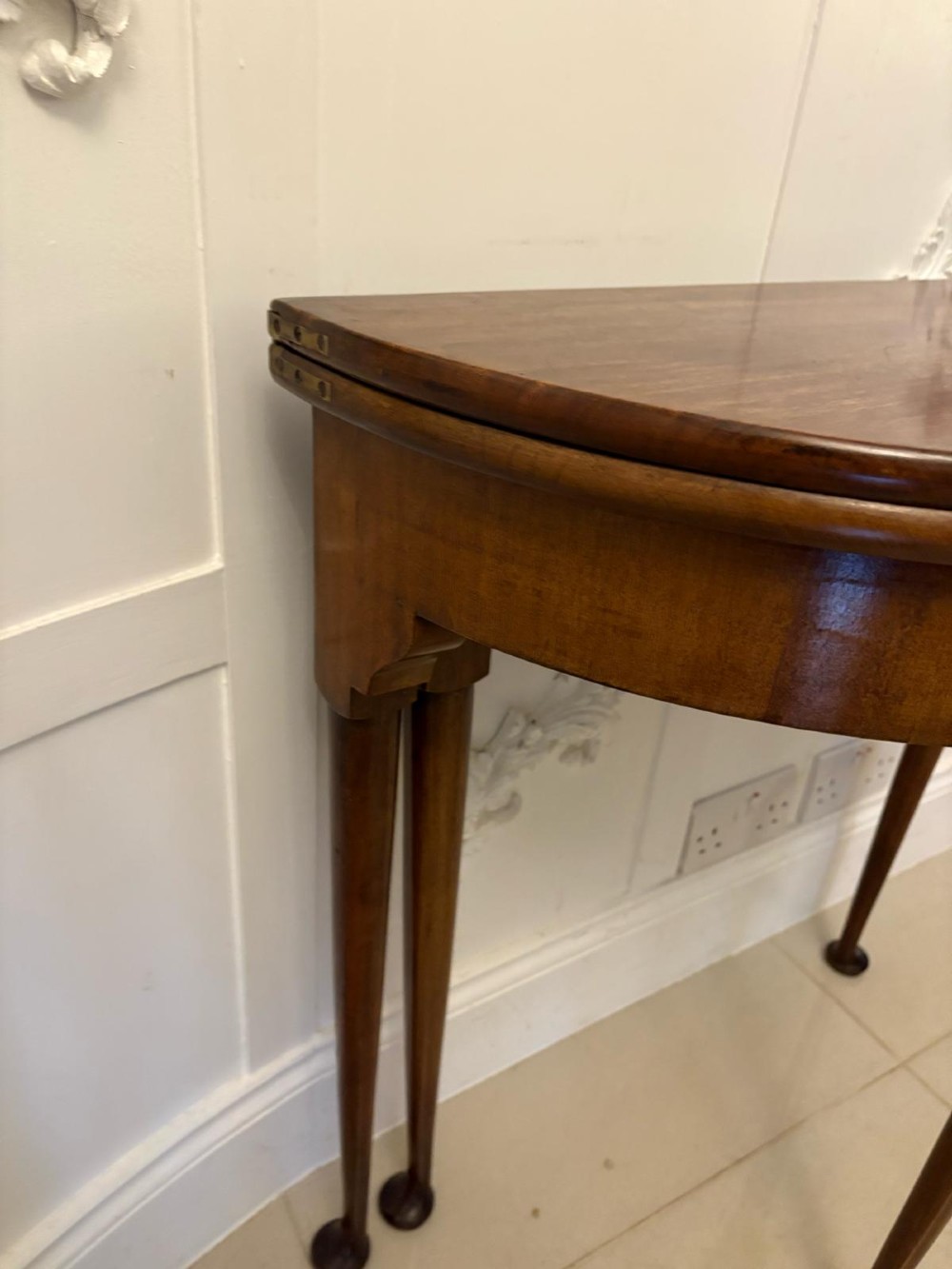 An antique warm brown mahogany demi-lune card table featuring tapered legs with pad feet and a fold-over top. View X