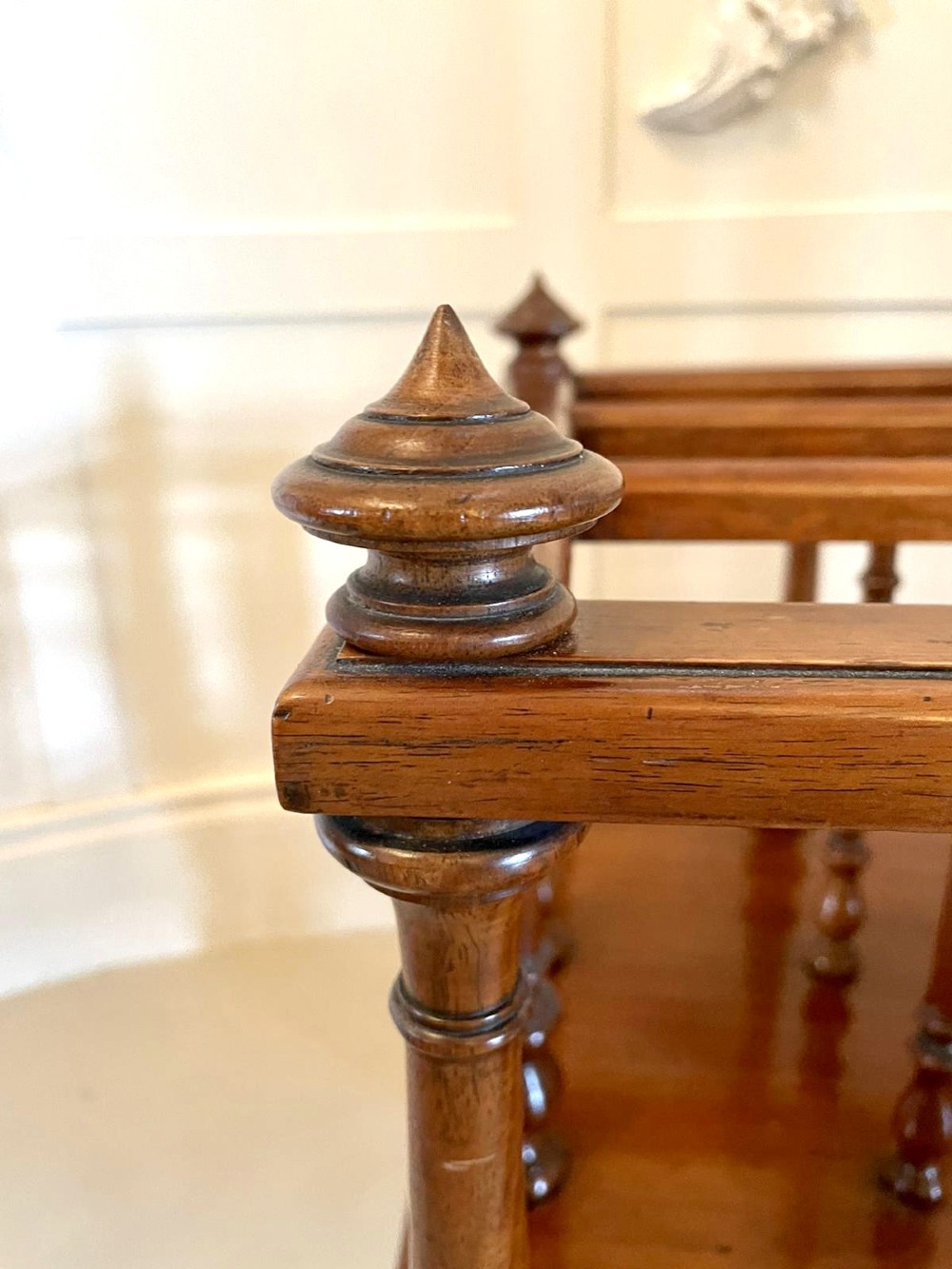 A Victorian figured walnut Canterbury featuring multiple vertical turned spindles, corner finials, a lower base drawer with two knobs, and brass castors. View II