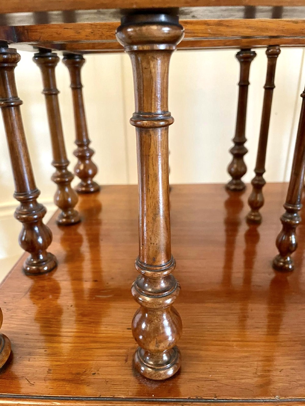 A Victorian figured walnut Canterbury featuring multiple vertical turned spindles, corner finials, a lower base drawer with two knobs, and brass castors. View VII