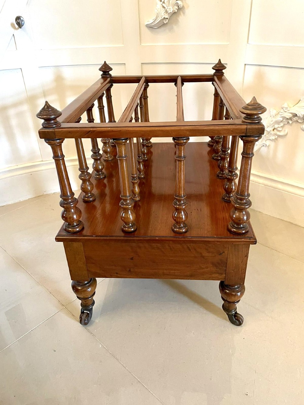 A Victorian figured walnut Canterbury featuring multiple vertical turned spindles, corner finials, a lower base drawer with two knobs, and brass castors. View VIII