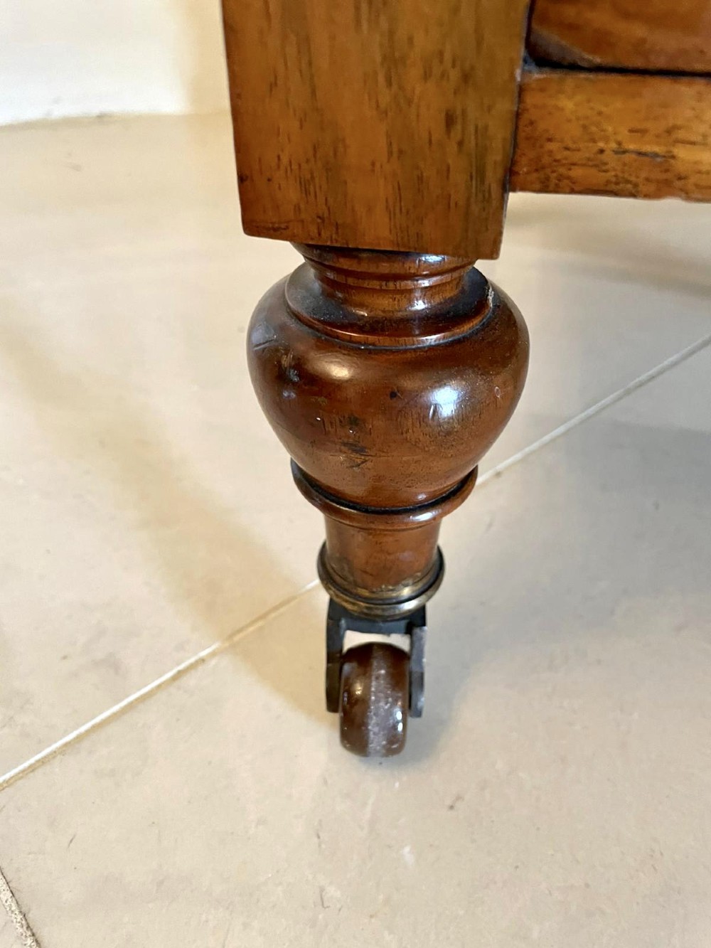 A Victorian figured walnut Canterbury featuring multiple vertical turned spindles, corner finials, a lower base drawer with two knobs, and brass castors. View XII
