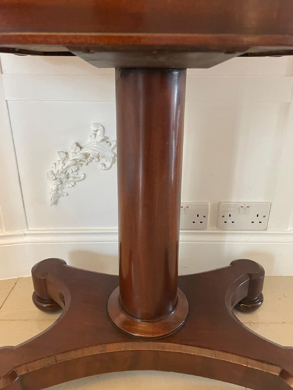 A Victorian mahogany card table featuring a rectangular fold-over top, carved scroll apron brackets, and a central cylindrical pedestal on a four-point plinth base. View II