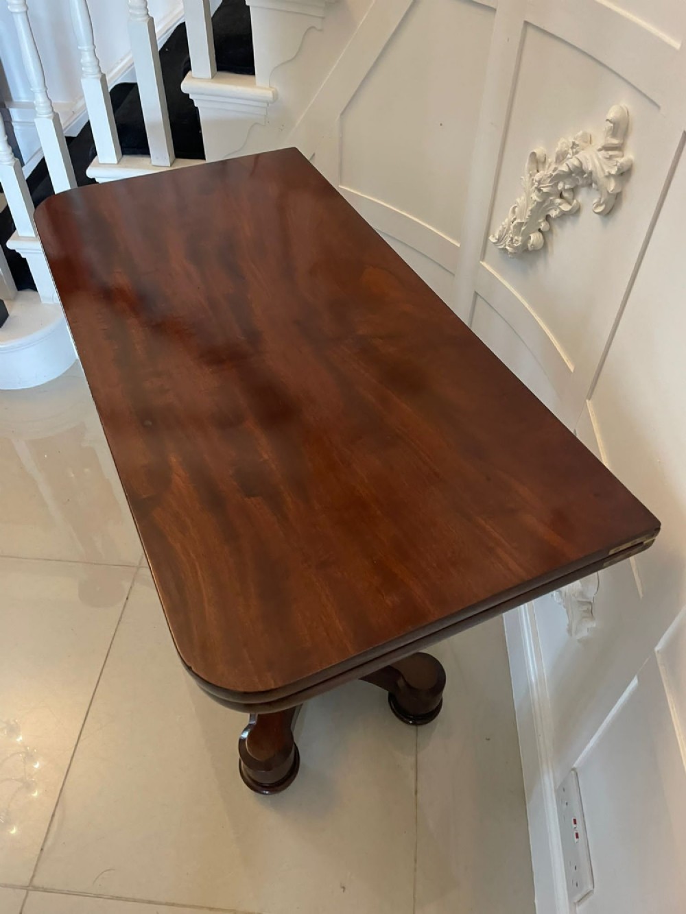 A Victorian mahogany card table featuring a rectangular fold-over top, carved scroll apron brackets, and a central cylindrical pedestal on a four-point plinth base. View III