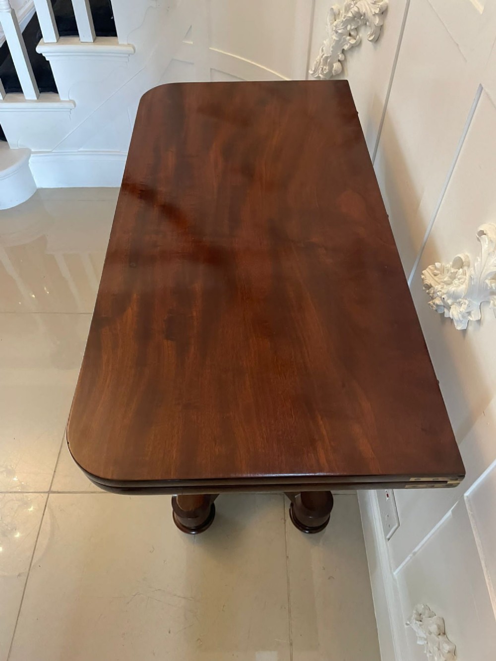 A Victorian mahogany card table featuring a rectangular fold-over top, carved scroll apron brackets, and a central cylindrical pedestal on a four-point plinth base. View IV