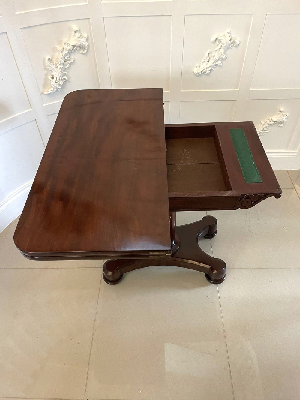 A Victorian mahogany card table featuring a rectangular fold-over top, carved scroll apron brackets, and a central cylindrical pedestal on a four-point plinth base. View V