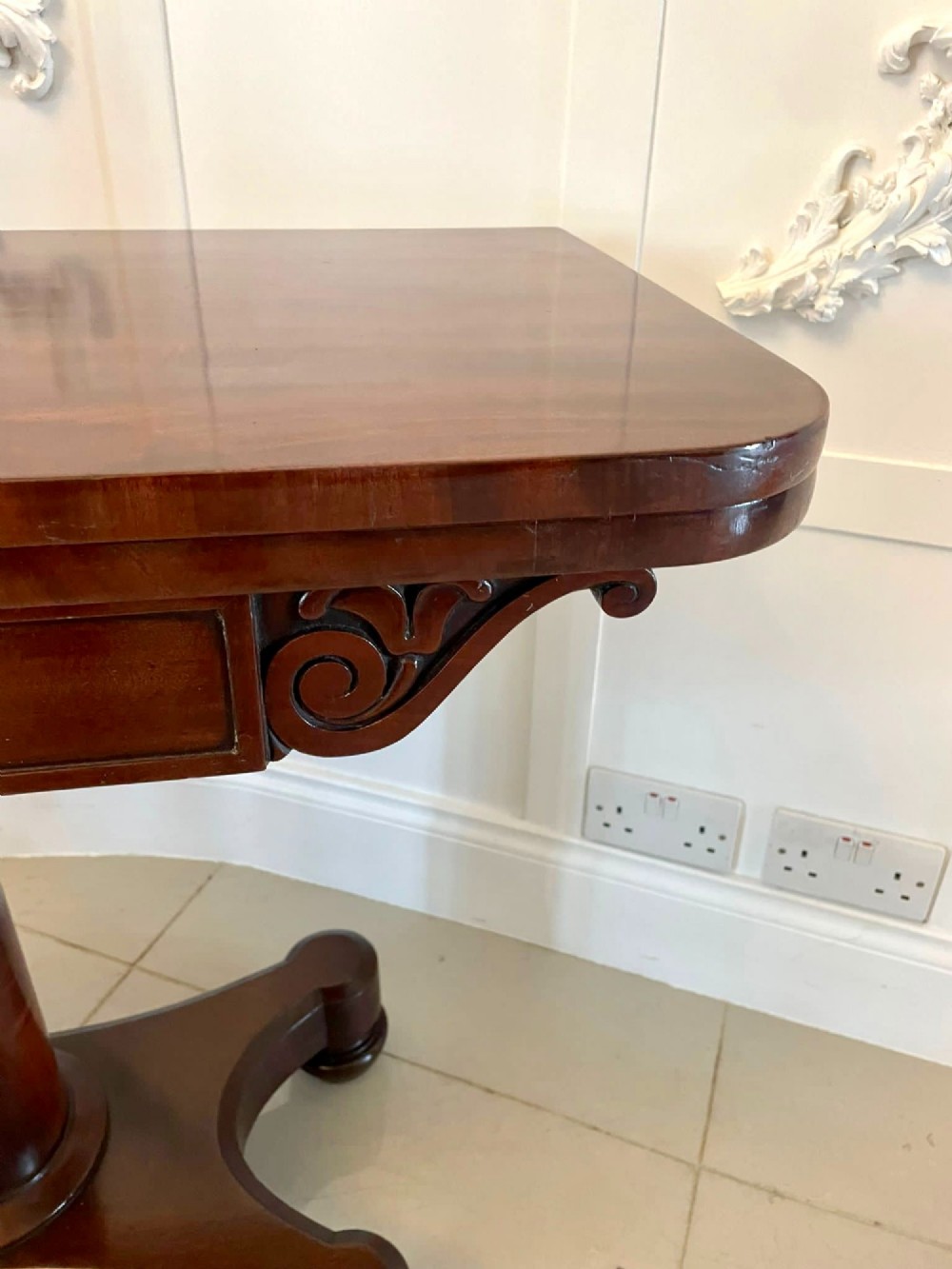 A Victorian mahogany card table featuring a rectangular fold-over top, carved scroll apron brackets, and a central cylindrical pedestal on a four-point plinth base. View XI