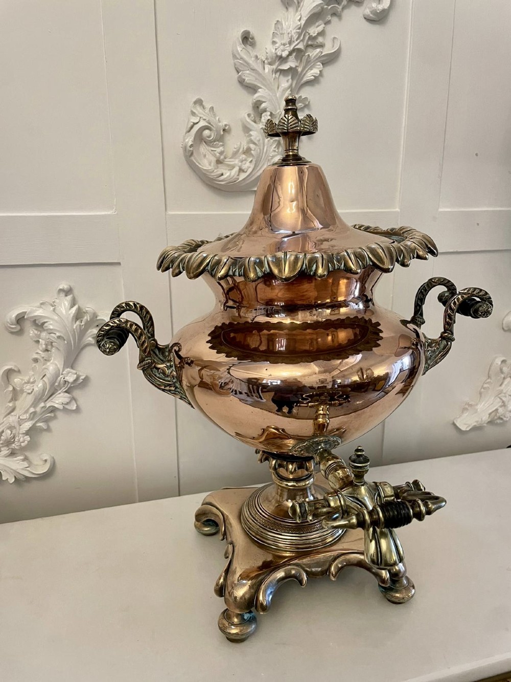 An antique Victorian polished copper and brass samovar featuring cast scrolling handles, a fluted top lid, a front tap, and a stepped square base. View VII