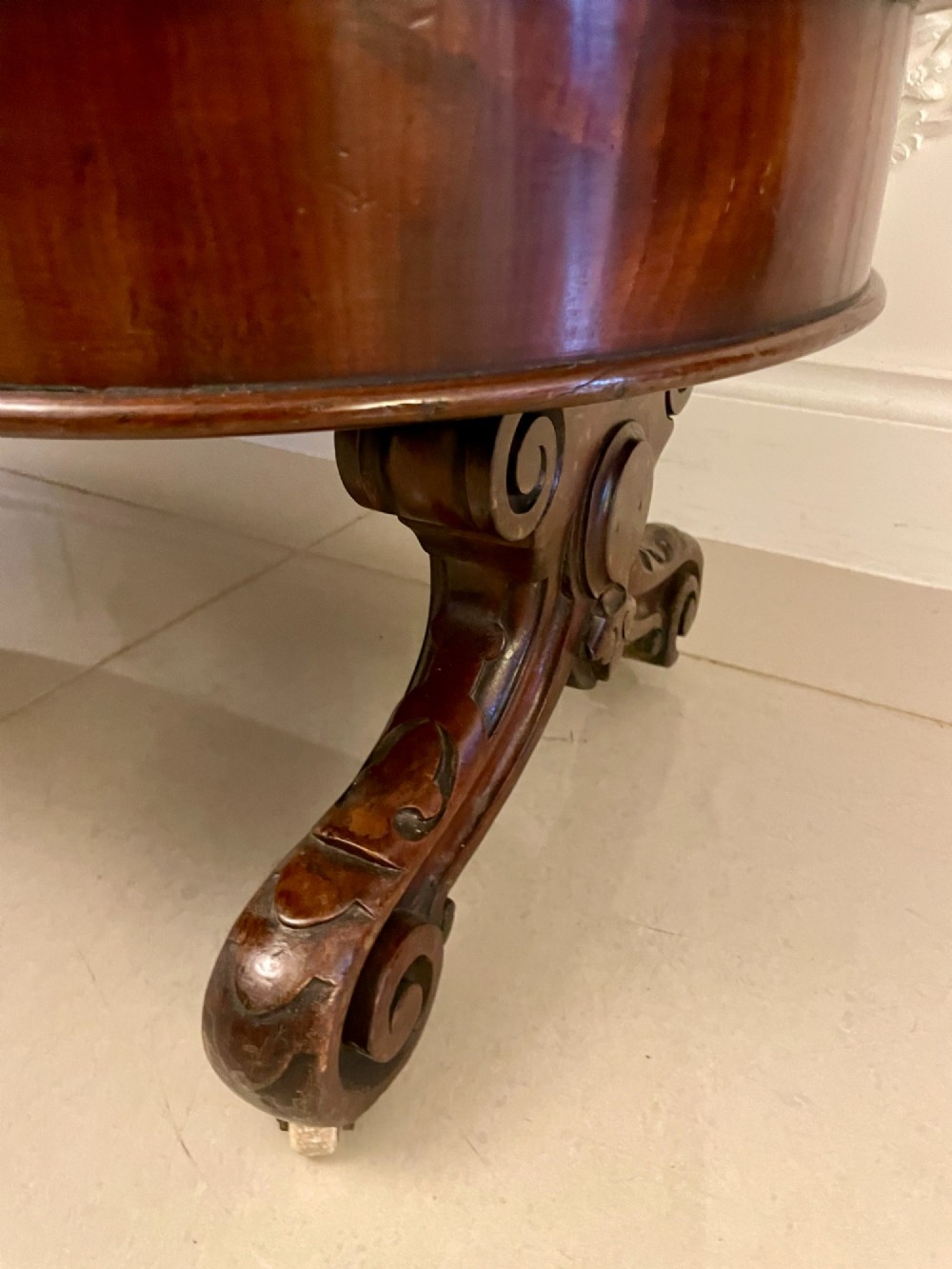 A two-tiered oval mahogany console table featuring carved column supports, a smooth polished finish, and castors on scroll feet. View VII