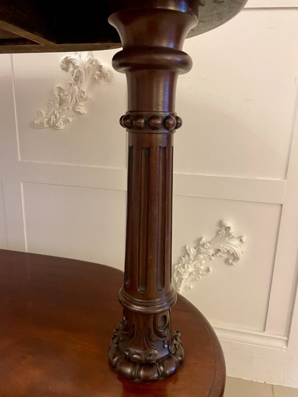 A two-tiered oval mahogany console table featuring carved column supports, a smooth polished finish, and castors on scroll feet. View VIII