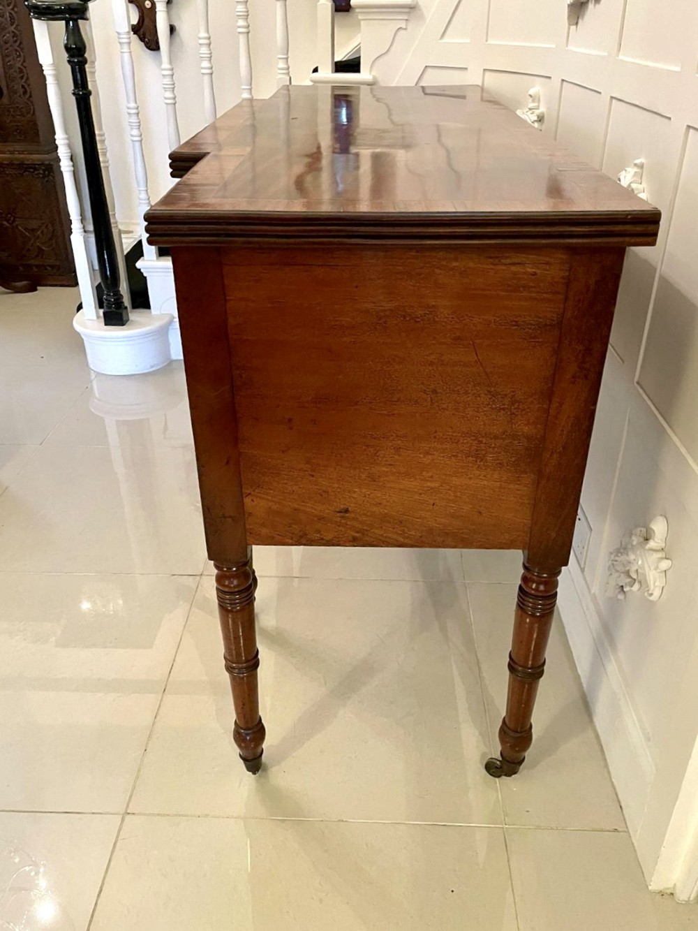 A Regency period mahogany breakfront sideboard featuring brass inlay motifs, a central drawer flanked by cupboards, turned legs, and brass castors. View II